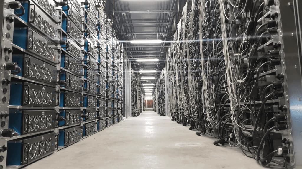 Inside view of a generic modern data center, showing a hallway of server racks illuminated by bright white lights.